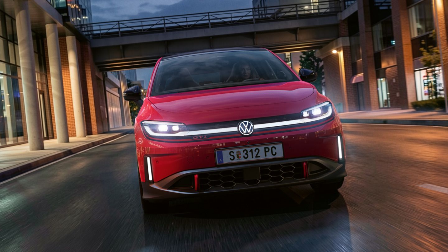 Eine Person fährt einen roten VW ID. Polo GTI durch ein modern beleuchtetes Geschäftsviertel am Abend.