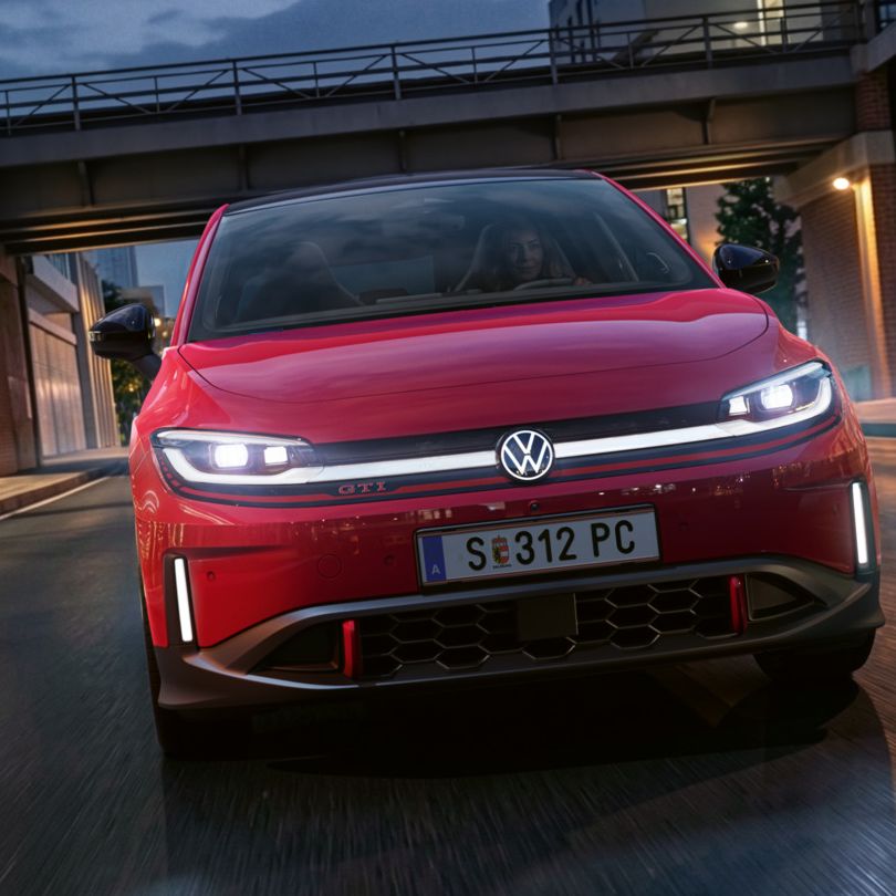 Eine Person fährt einen roten VW ID. Polo GTI durch ein modern beleuchtetes Geschäftsviertel am Abend.