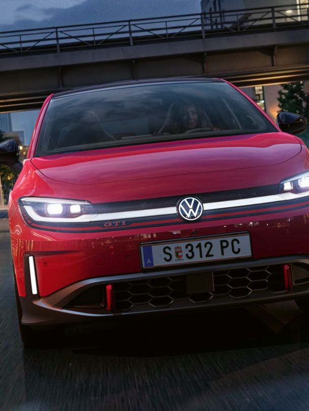 Eine Person fährt einen roten VW ID. Polo GTI durch ein modern beleuchtetes Geschäftsviertel am Abend.