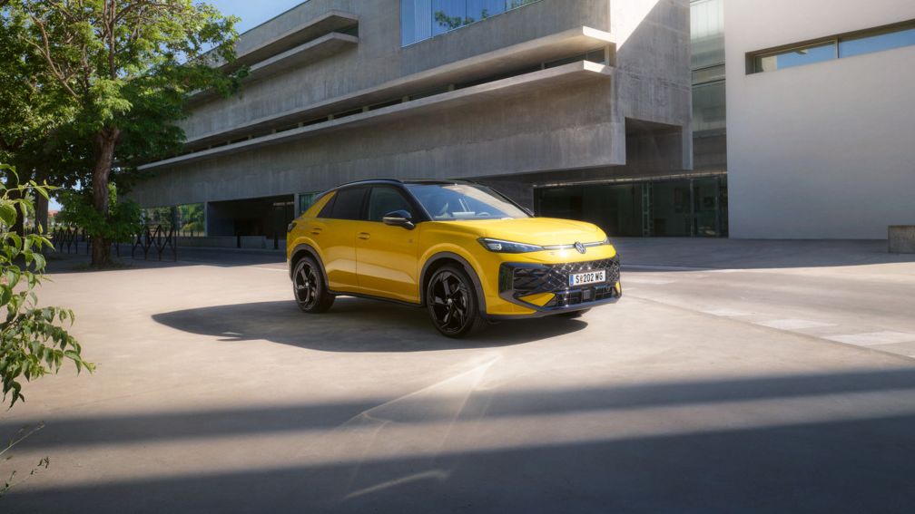 Ein gelber T-Roc R-Line steht vor einem modernen Gebäude mit Beton-Architektur.