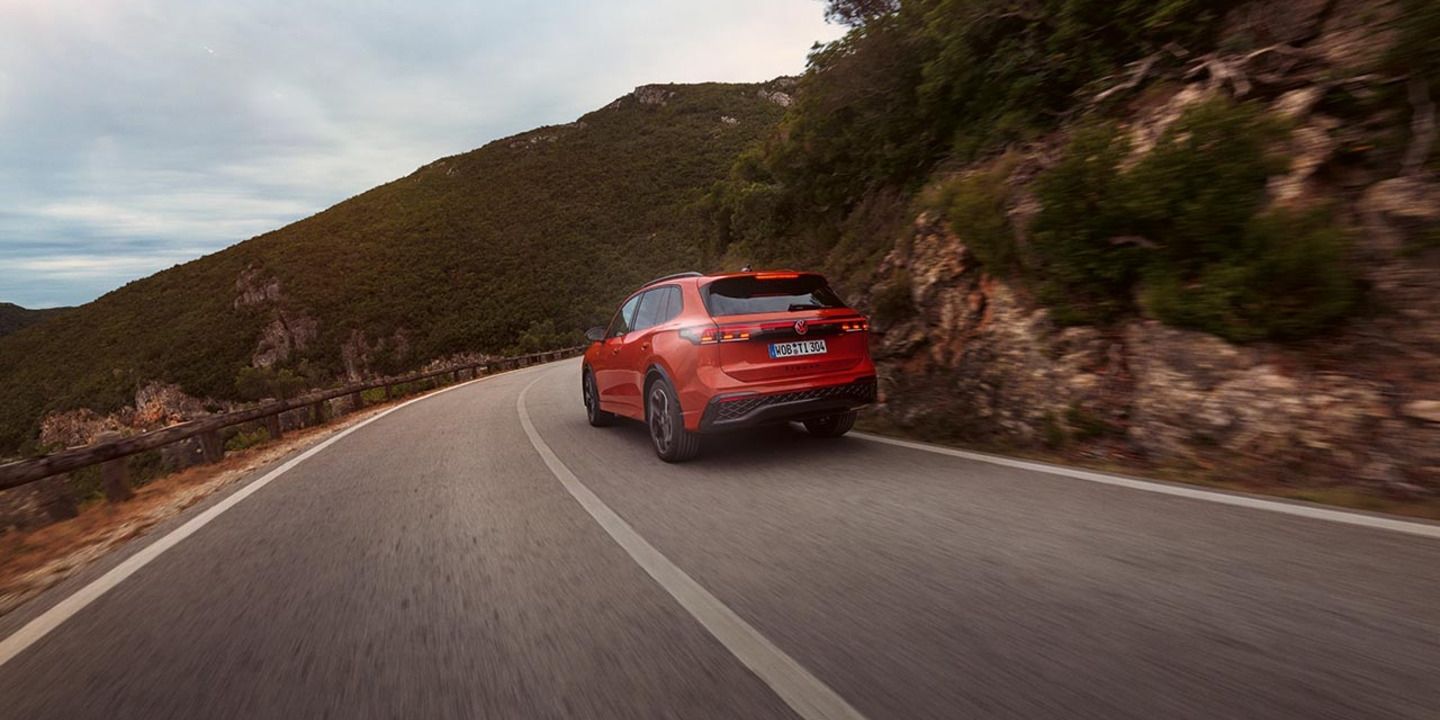 Roter VW Tiguan in Heckansicht fährt durch eine bergige Landschaft.