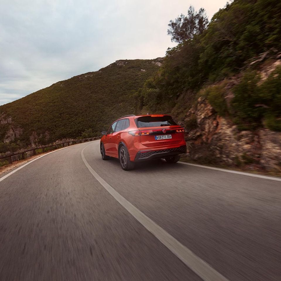 Roter VW Tiguan in Heckansicht fährt durch eine bergige Landschaft.