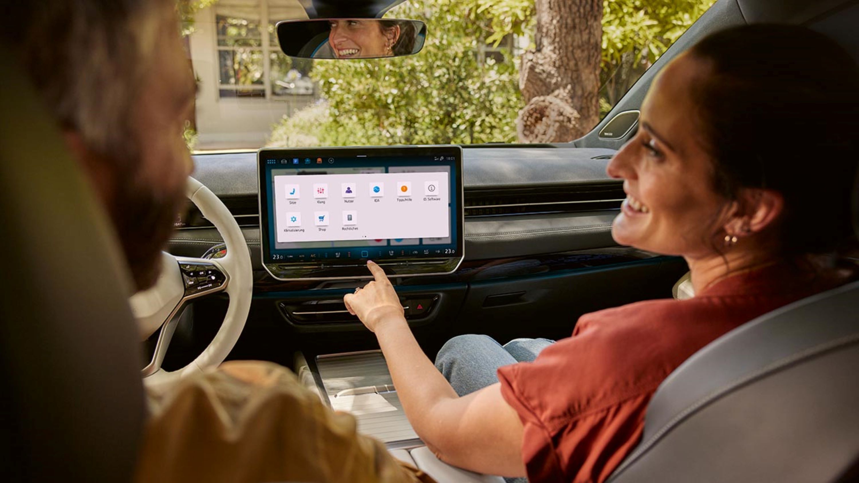 Ein Mann und eine Frau sitzen vorn im VW ID.7, die Frau zeigt auf das Menü im Infotainment-System.