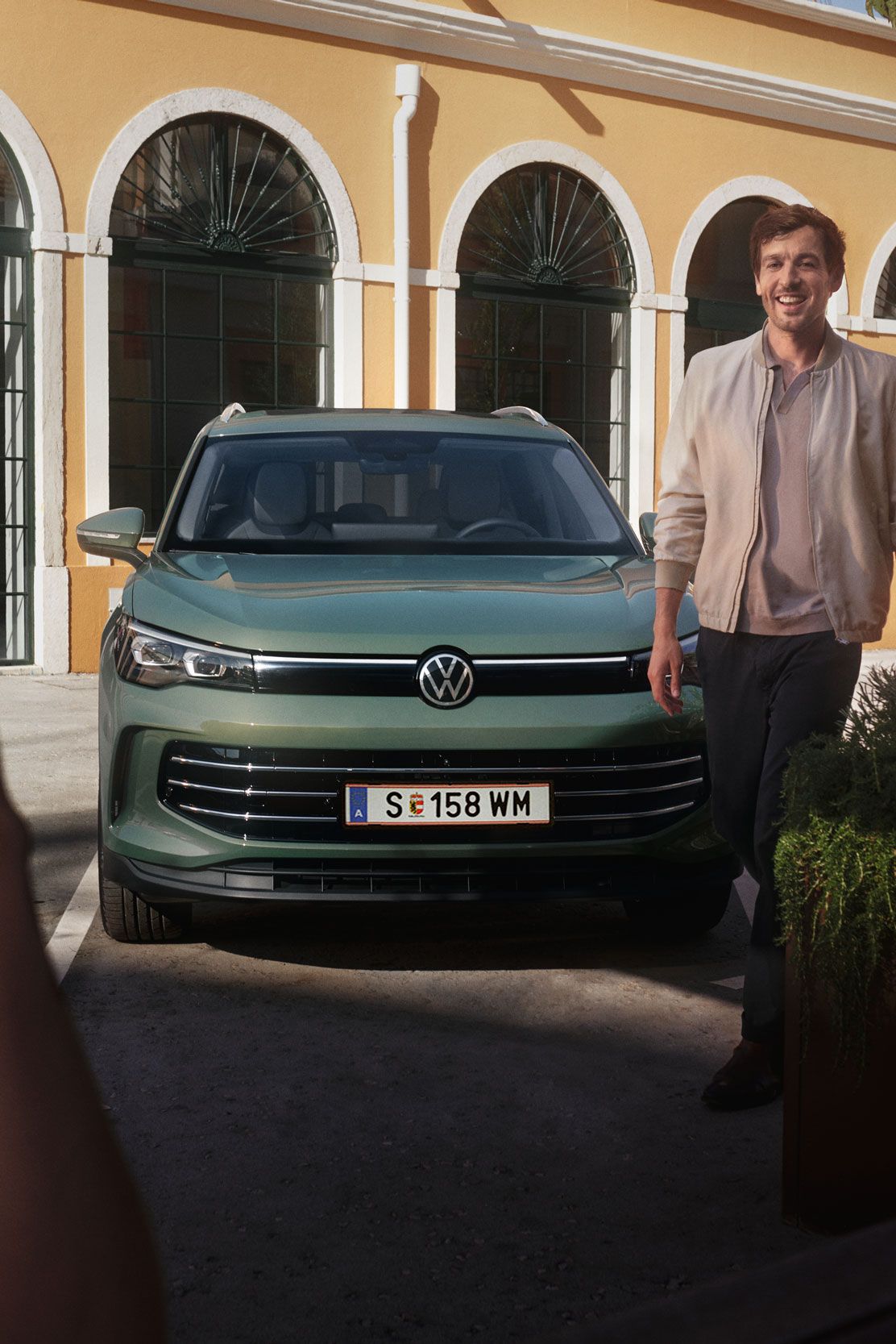 Tiguan ist vor einem Haus auf einem Parkplatz geparkt von dem ein Mann weggeht und ihn im Vordergrund währenddessen eine Frau anssieht.