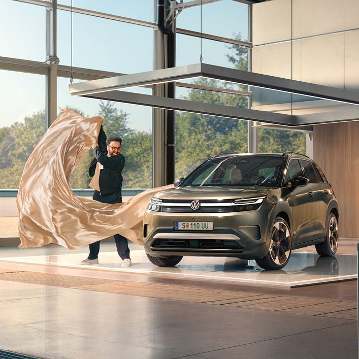 Ein Mann zieht ein großes Tuch von einem grünen VW ID. Cross, der in einem minimalistisch eingerichteten Designstudio steht.