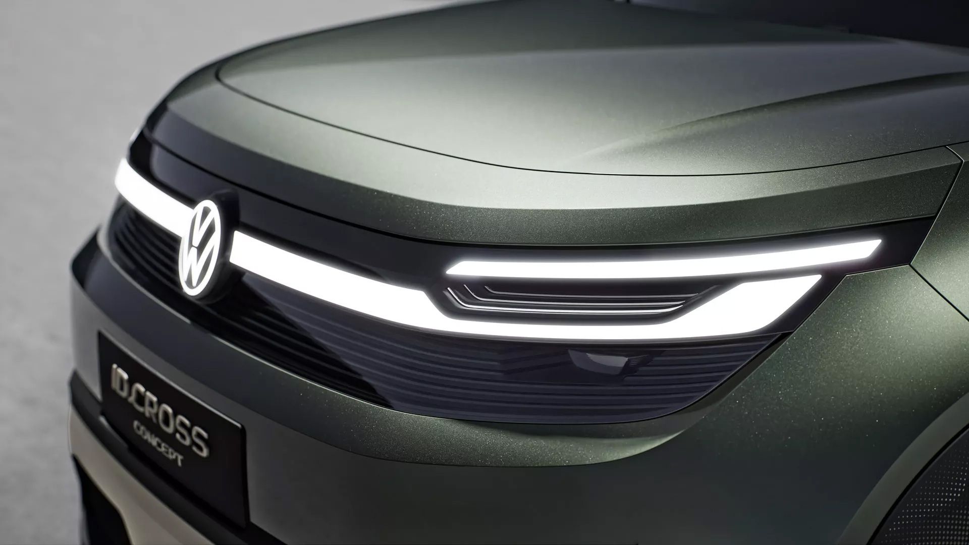 Ein modernes Autoscheinwerferdesign vom VW ID. Cross, mit leuchtenden LED-Streifen und einer glänzenden Oberfläche. Das Auto hat eine dunkelgrüne Lackierung. Auf dem Nummernschild steht "I.D. CROZZ concept".
