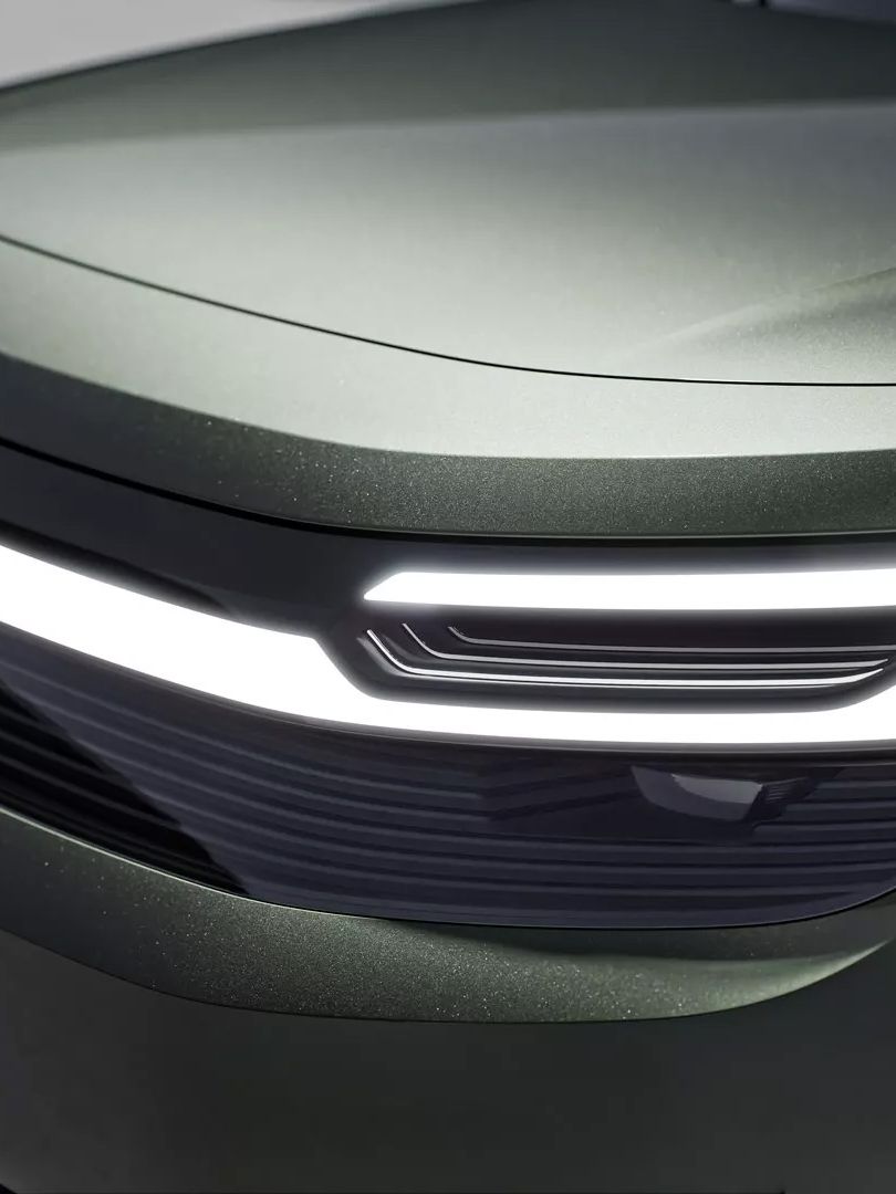 Ein modernes Autoscheinwerferdesign vom VW ID. Cross, mit leuchtenden LED-Streifen und einer glänzenden Oberfläche. Das Auto hat eine dunkelgrüne Lackierung. Auf dem Nummernschild steht "I.D. CROZZ concept".