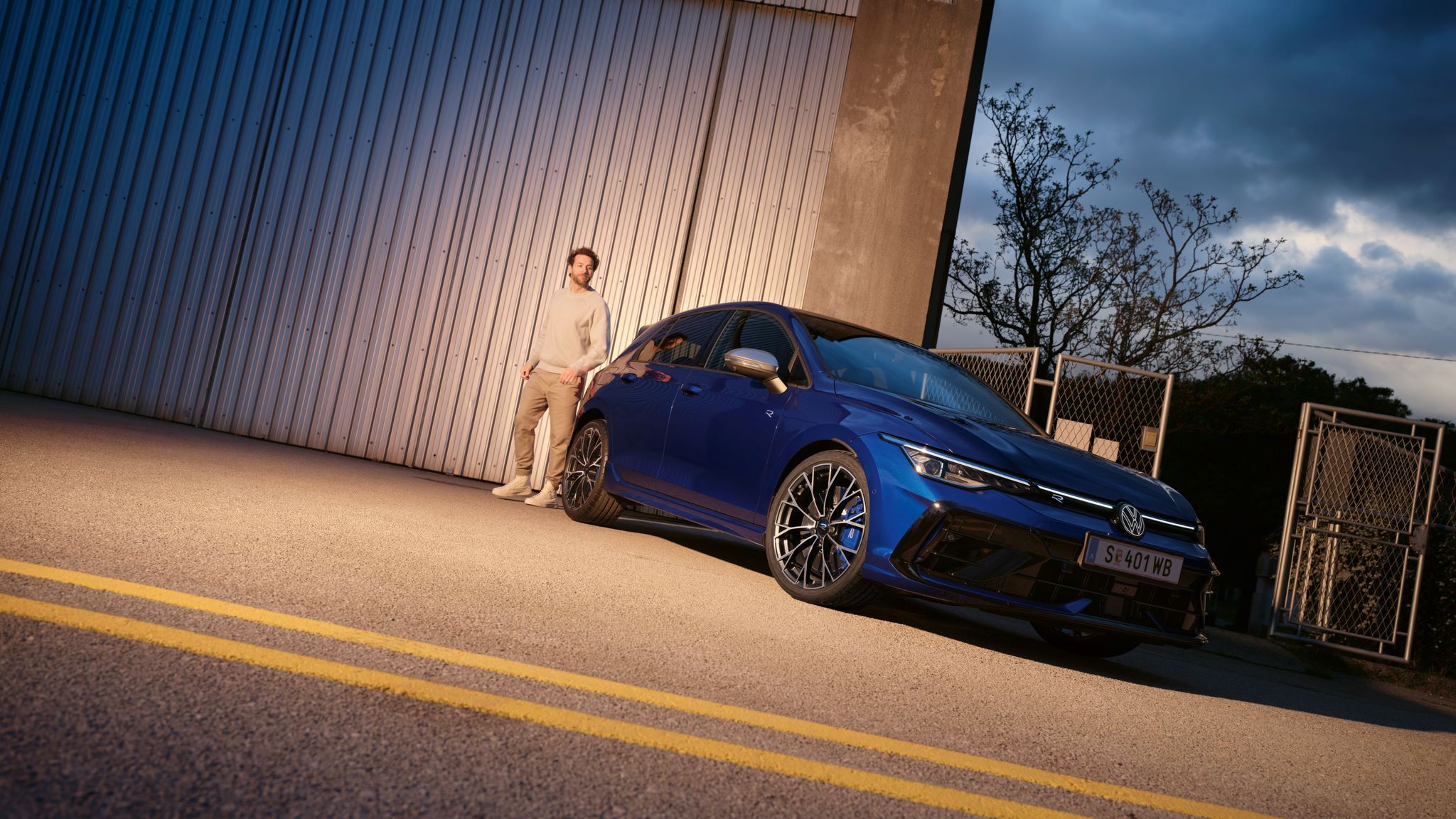 Golf R geparkt neben einer Halle, Mensch steht am Heck.
