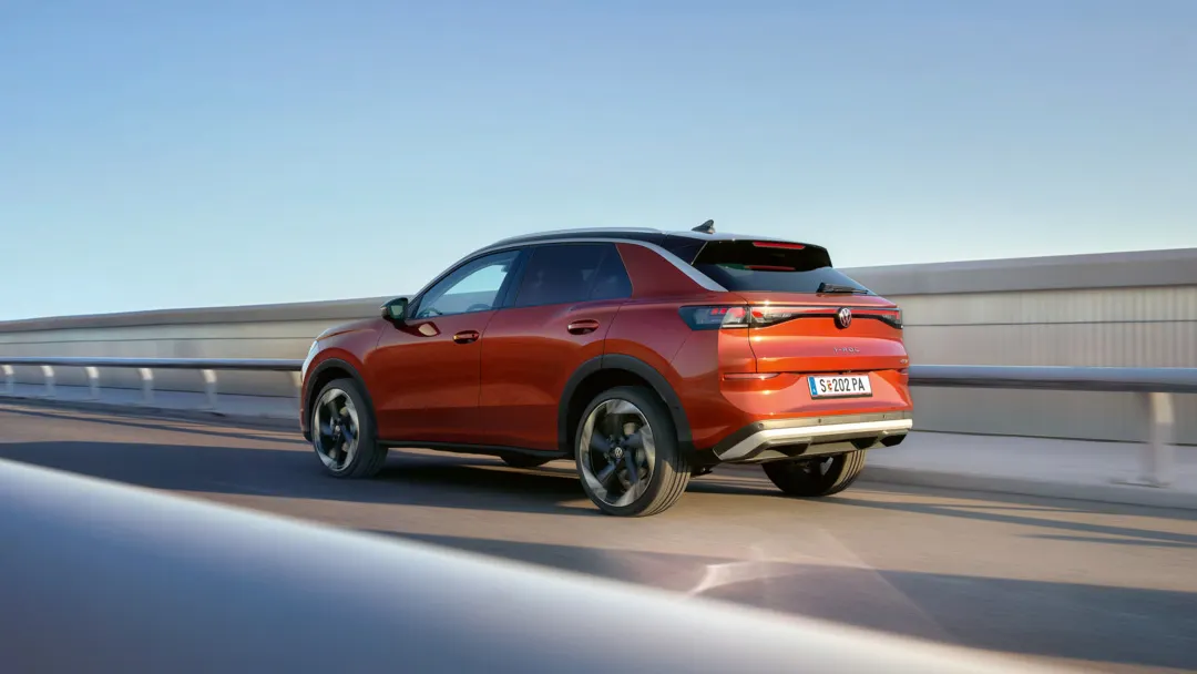 Ein roter T-Roc fährt auf einer offenen Straße bei sonnigem Wetter. Das Fahrzeug ist modern gestaltet und hat schwarze Felgen. Im Hintergrund sieht man den strahlend blauen Himmel.