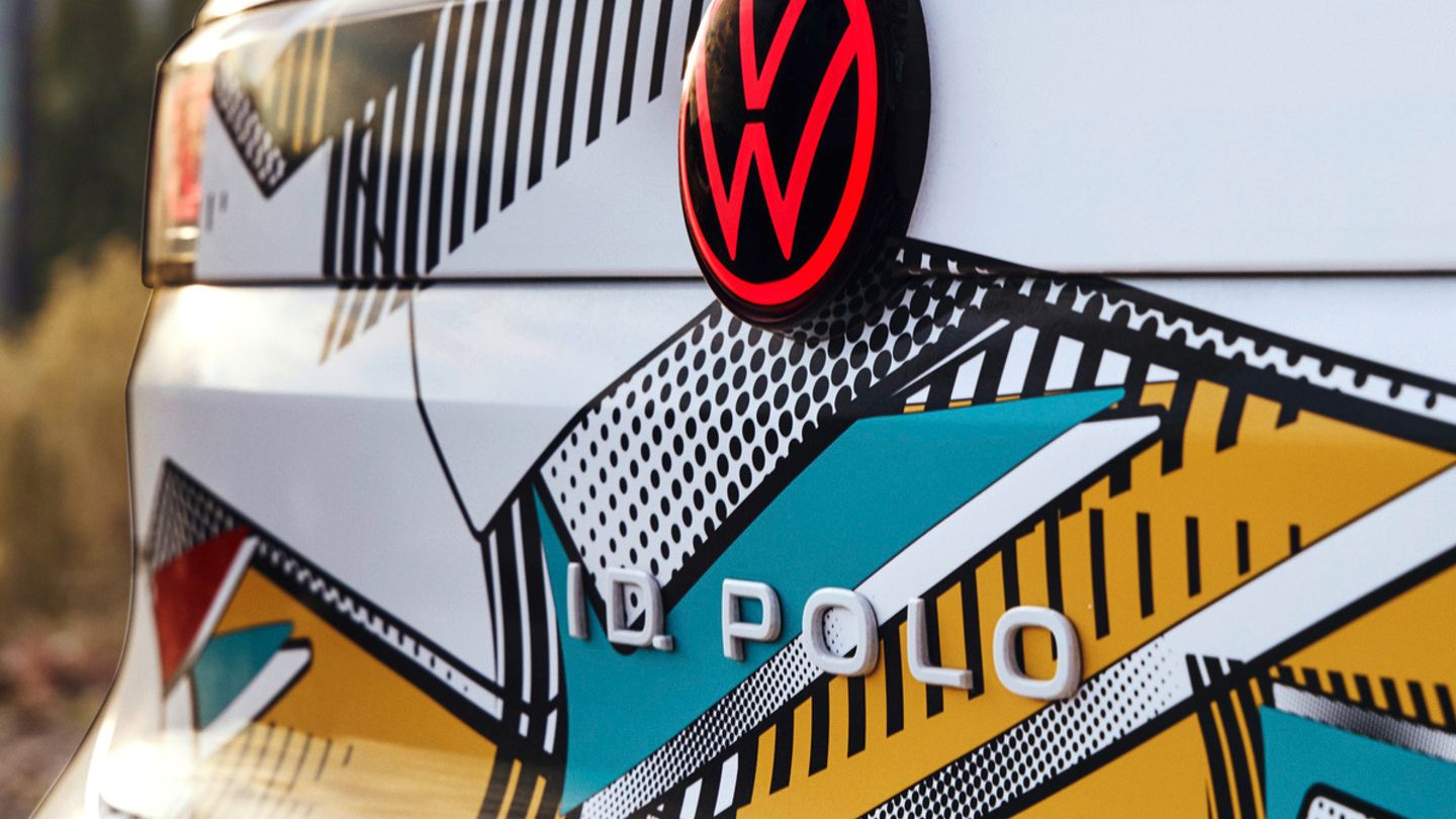 Nahaufnahme eines Volkswagen ID. Polo mit farbigem geometrischen Muster auf der Karosserie. Das VW-Logo ist rot und hebt sich deutlich von den Mustern ab. Im Hintergrund sind unscharf natürliche Elemente zu sehen.