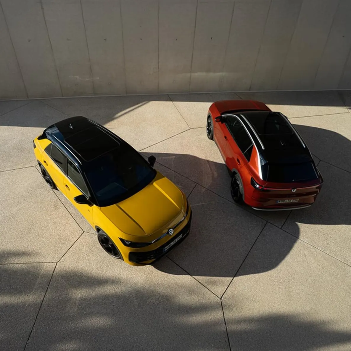 Ein gelber VW T-Roc R-Line und ein roter VW T-Roc Style von schräg oben vor einem modernen Gebäude.