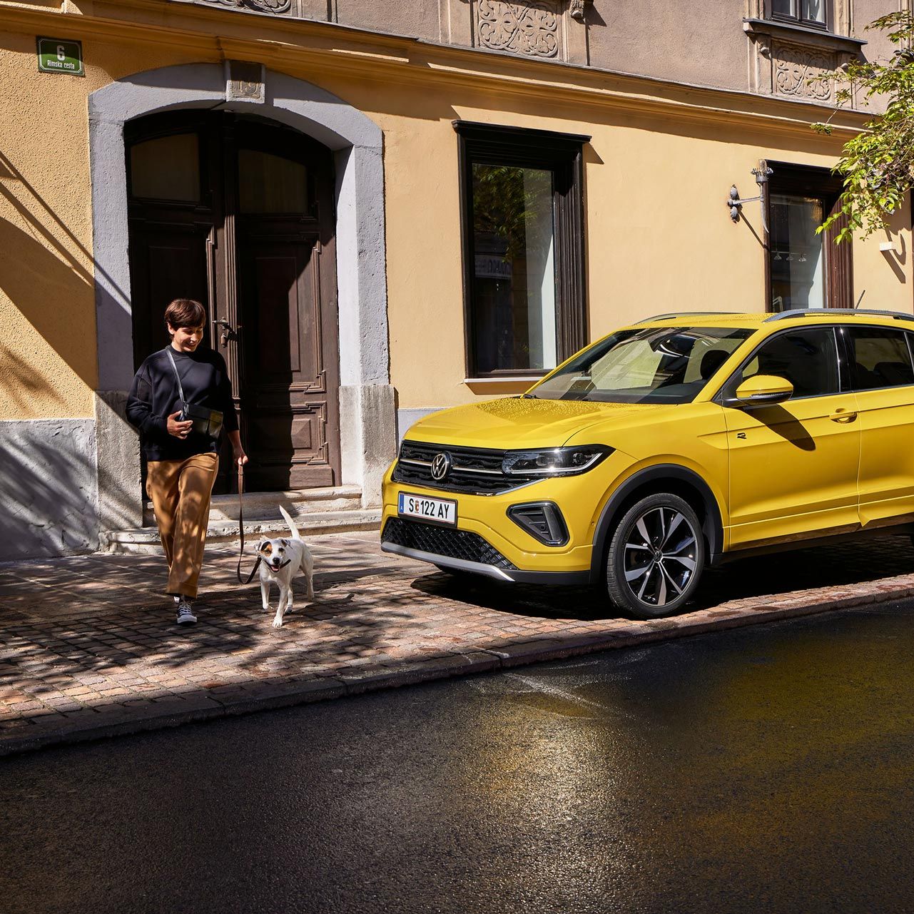 VW T-Cross parkt am Straßenrand, Frau mit kleinem Hund geht an ihm vorbei