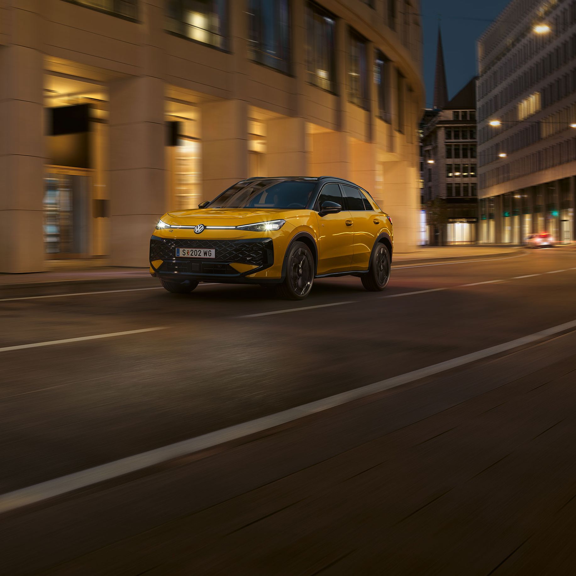 Ein gelber VW T-Roc R-Line fährt nachts durch eine urbane Umgebung.