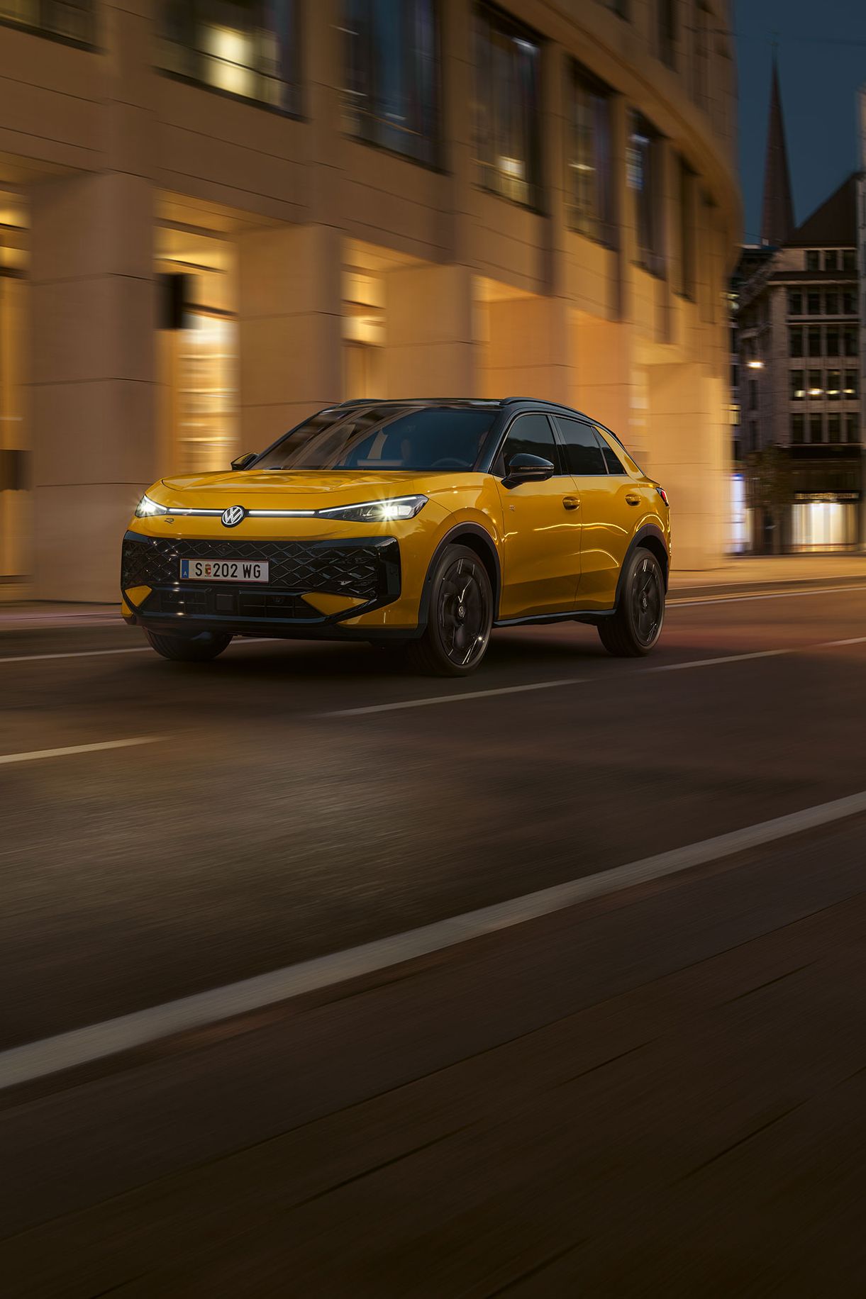 Ein gelber VW T-Roc R-Line fährt nachts durch eine urbane Umgebung.