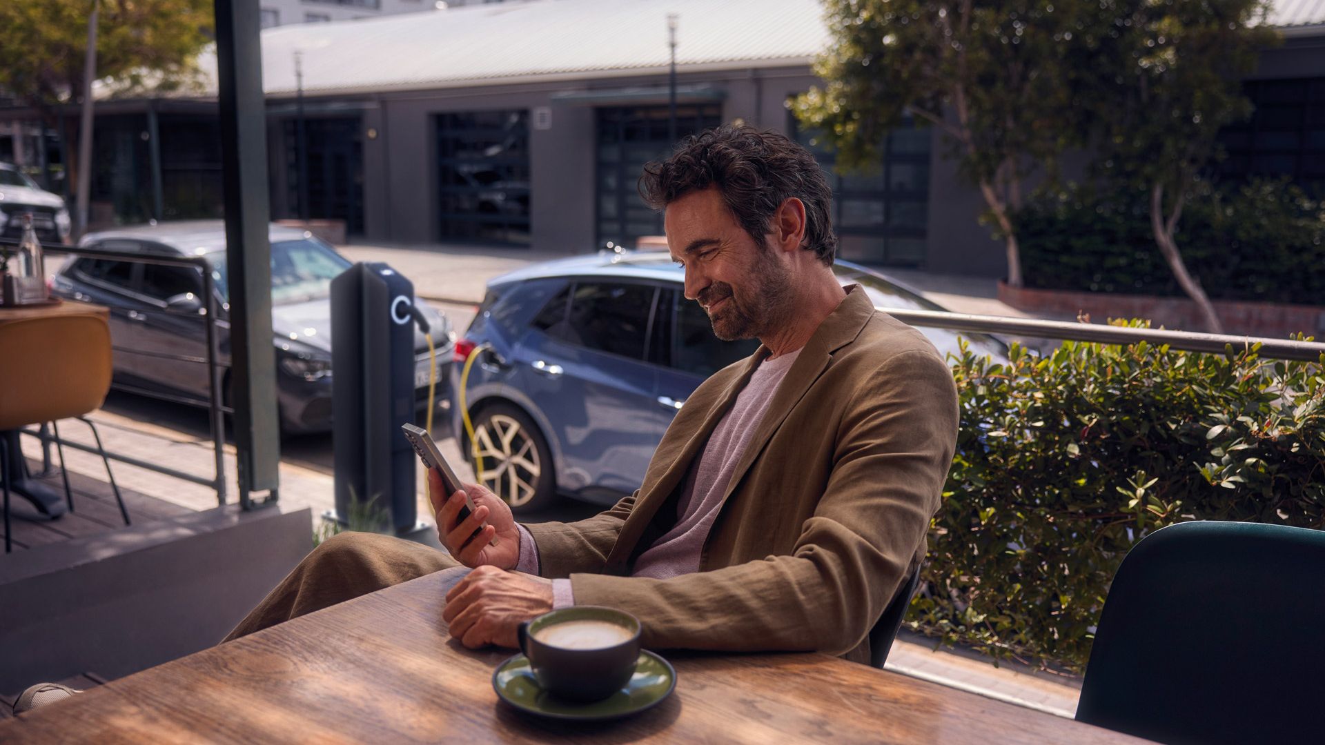 Ein Mann sitzt im Café und checkt per Smartphone den Ladestatus seines VW ID.3 Neo