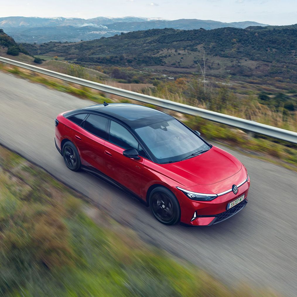 Blick auf die aerodynamisch gestaltete Front eines roten VW ID.7 GTX, der durch eine Berglandschaft fährt.