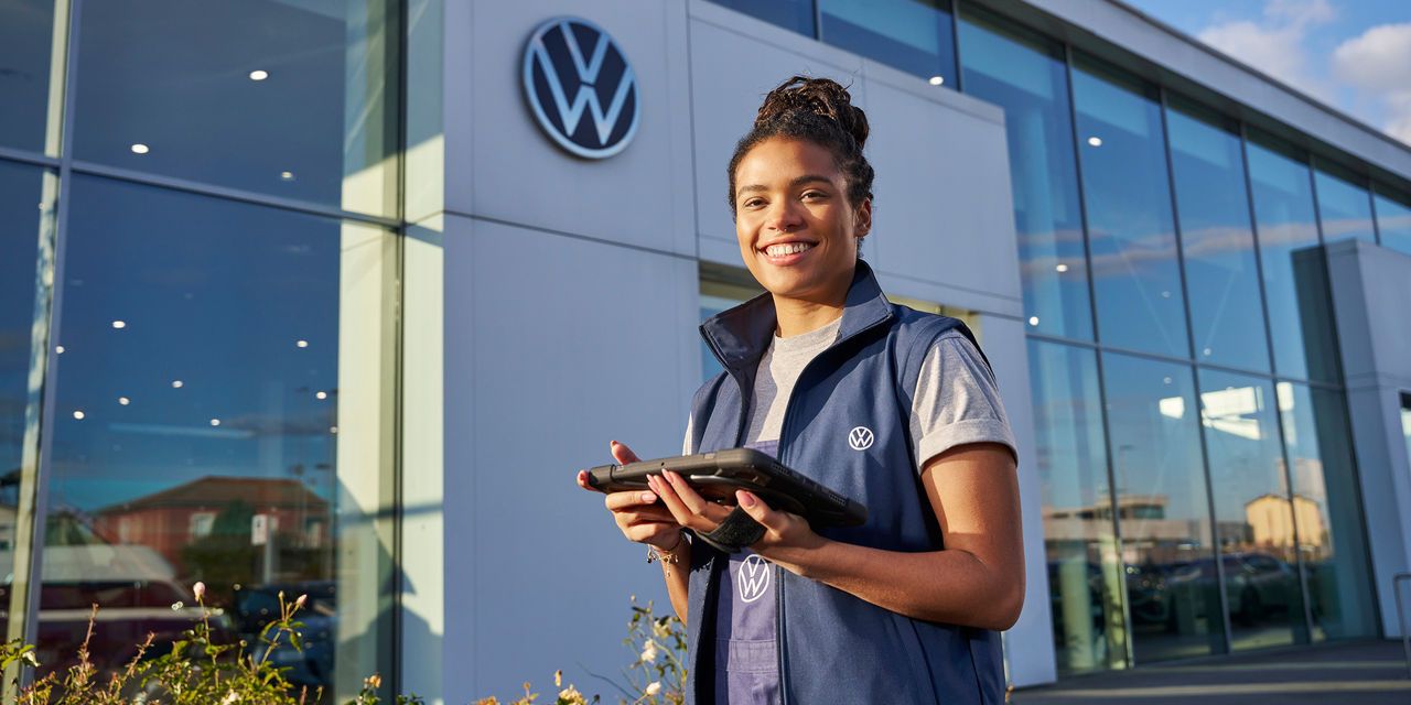 Servicefrau steht mit Tablet vor einem Volkswagen Partner Gebäude.