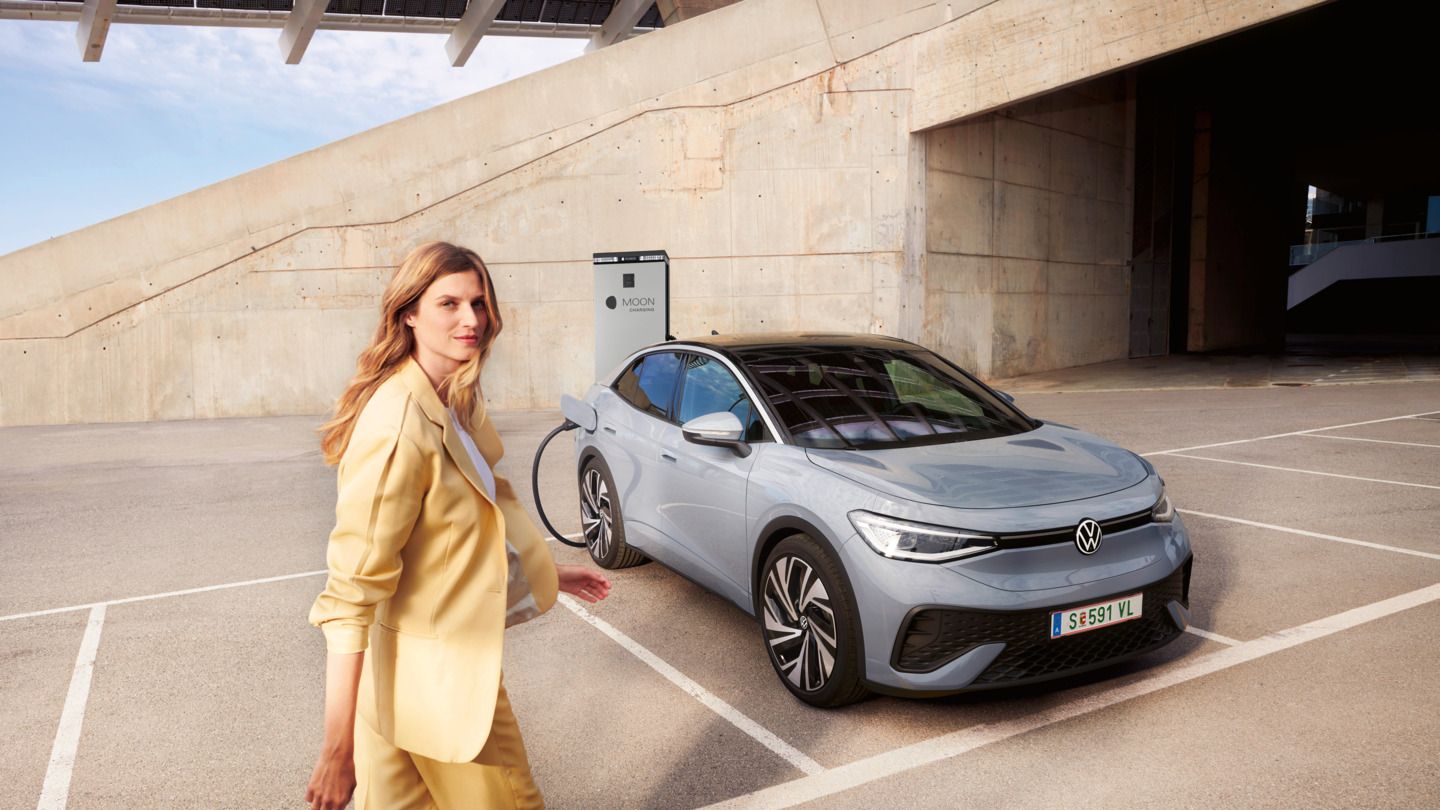 Eine Frau läuft zu einem grauen VW ID.5, der an einer MOON-Ladesäule aufgeladen wird. 