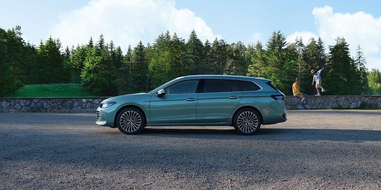 Ein grüner VW Passat B9 in der Seitenansicht, im Hintergrund zwei Menschen und Wald