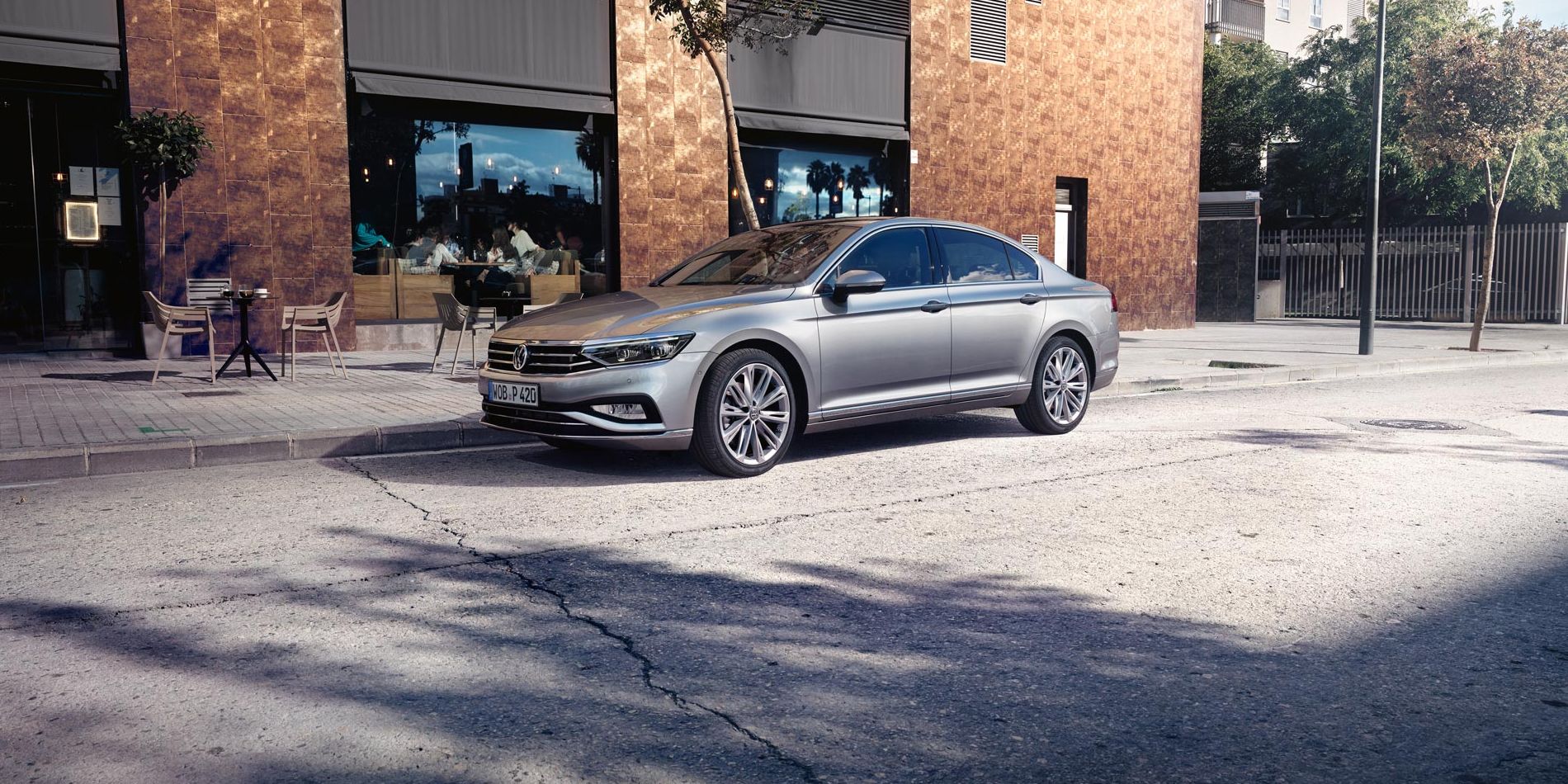 VW Passat steht auf einer Straße vor einem Café mit Sitzmöglichkeiten.