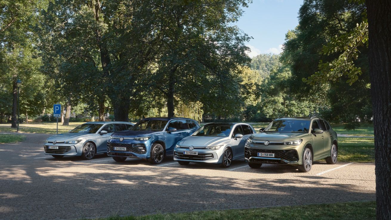 Vier VW Plug-In-Hybrid-Modelle stehen nebeneinander auf einem Parkplatz in einem Park.