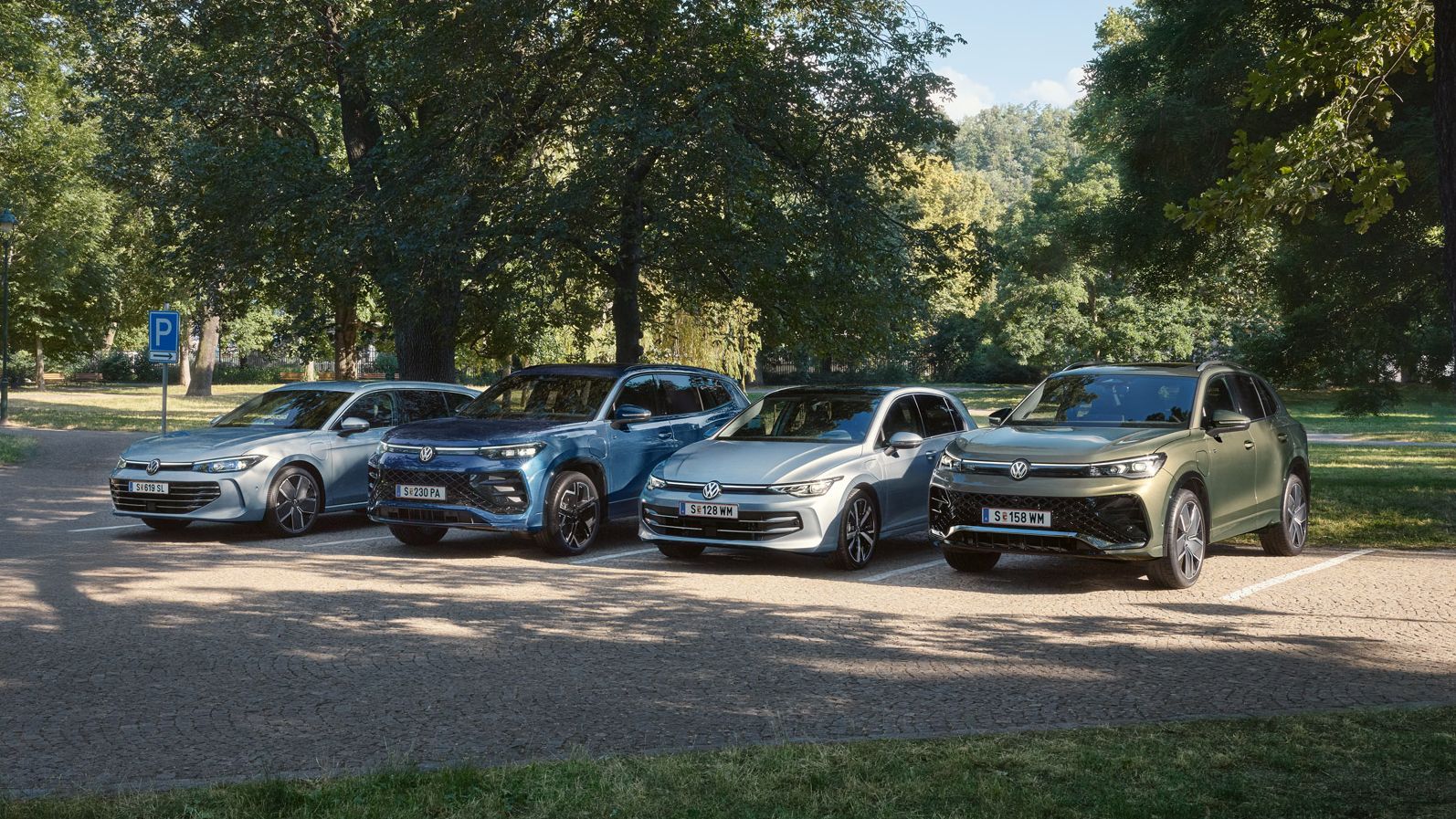 Vier VW Plug-In-Hybrid-Modelle stehen nebeneinander auf einem Parkplatz in einem Park.