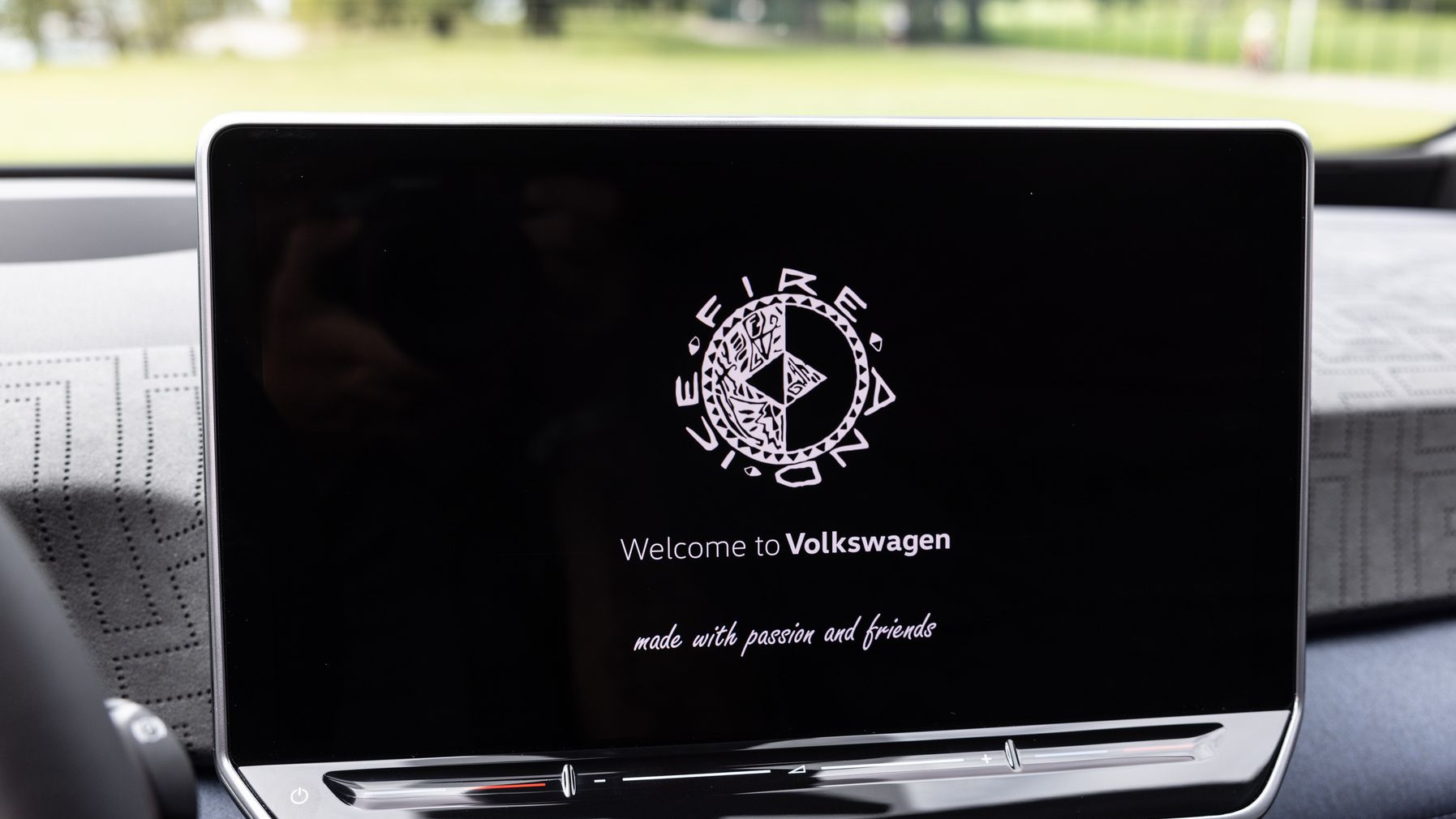 Ein Infotainment-Bildschirm in einem Volkswagen-Fahrzeug zeigt die Begrüßungsnachricht "Welcome to Volkswagen". Der Text lautet weiter "made with passion and friends". Das Display ist elegant und modern gestaltet.