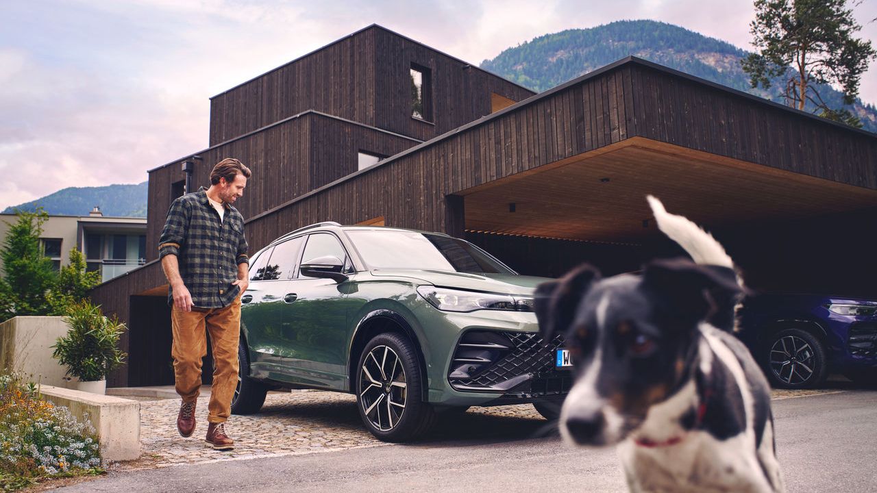 Ein grüner Volkswagen Tiguan steht in einer Hauseinfahrt. Ein Mann mit seinem Hund bewegt sich vom Fahrzeug fort.