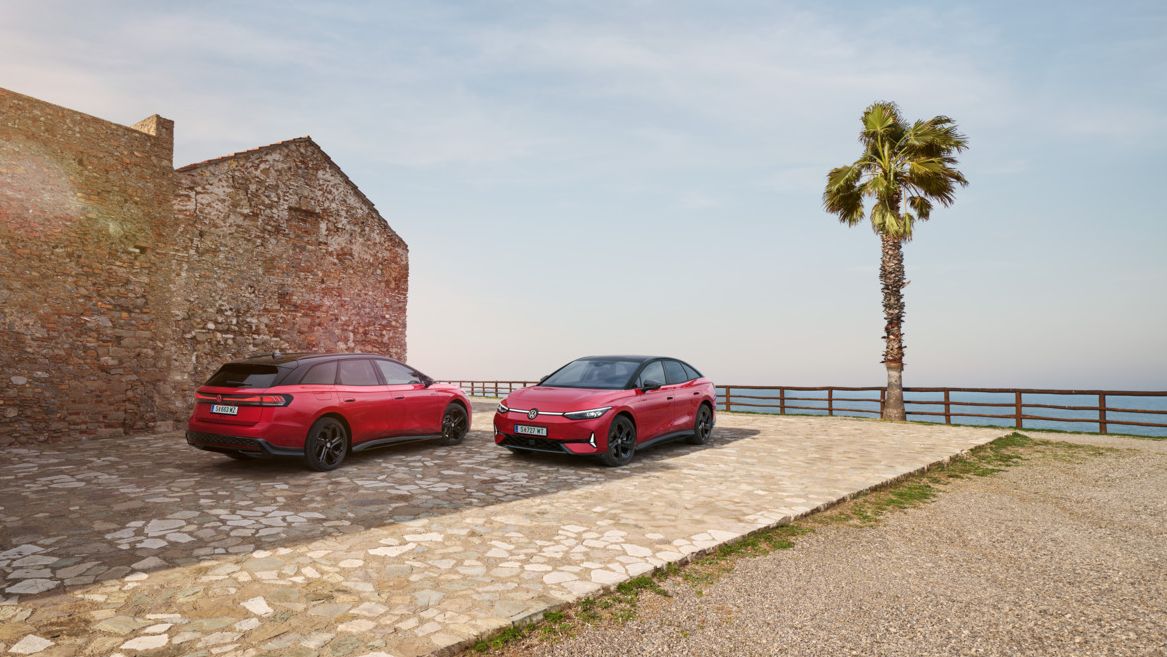 Ein roter ID.7 GTX und ID.7 Tourer GTX stehen nebeneinander vor einem Steinhaus mit Bick auf das Meer. 