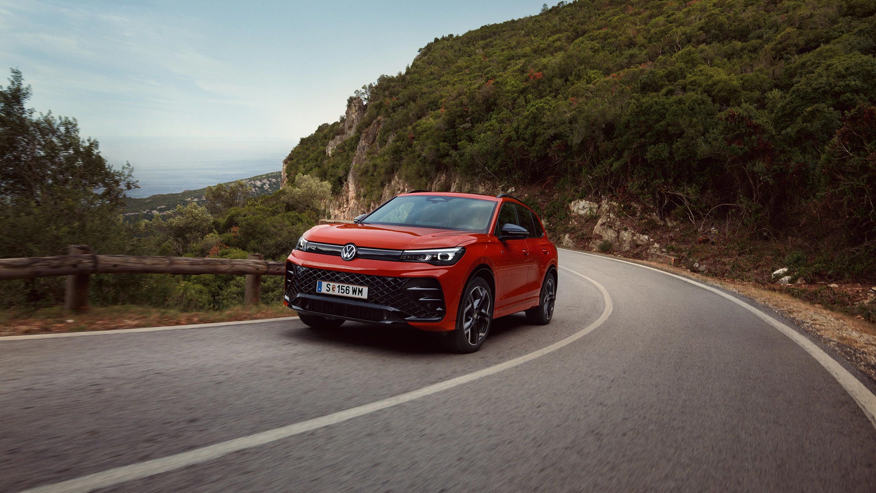 Roter VW Tiguan R-Line fährt eine kurvige Straße entlang.