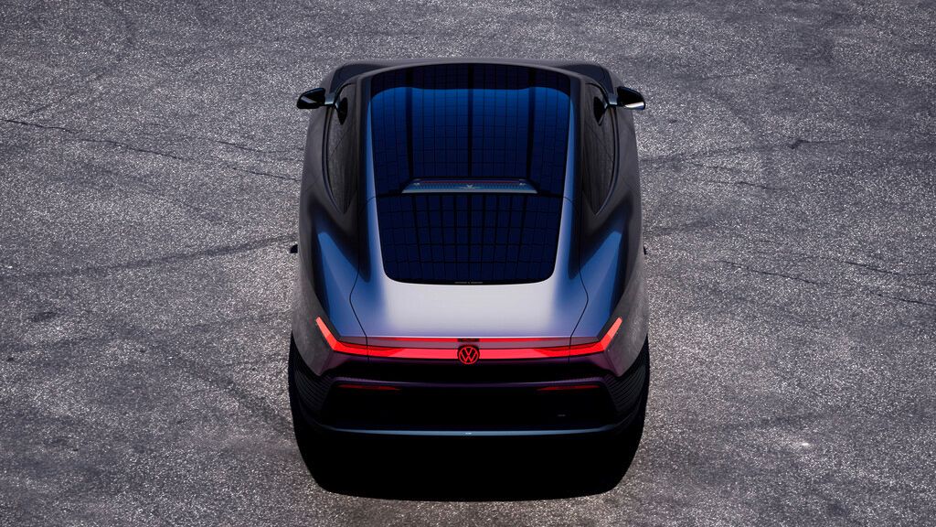 Rückansicht eines futuristischen, dunklen Elektroautos, das auf einer grauen Asphaltfläche steht. Das Fahrzeug hat ein durchgehendes rotes LED-Rücklicht und ein großes Glasdach, in dem sich ein Gittermuster spiegelt.