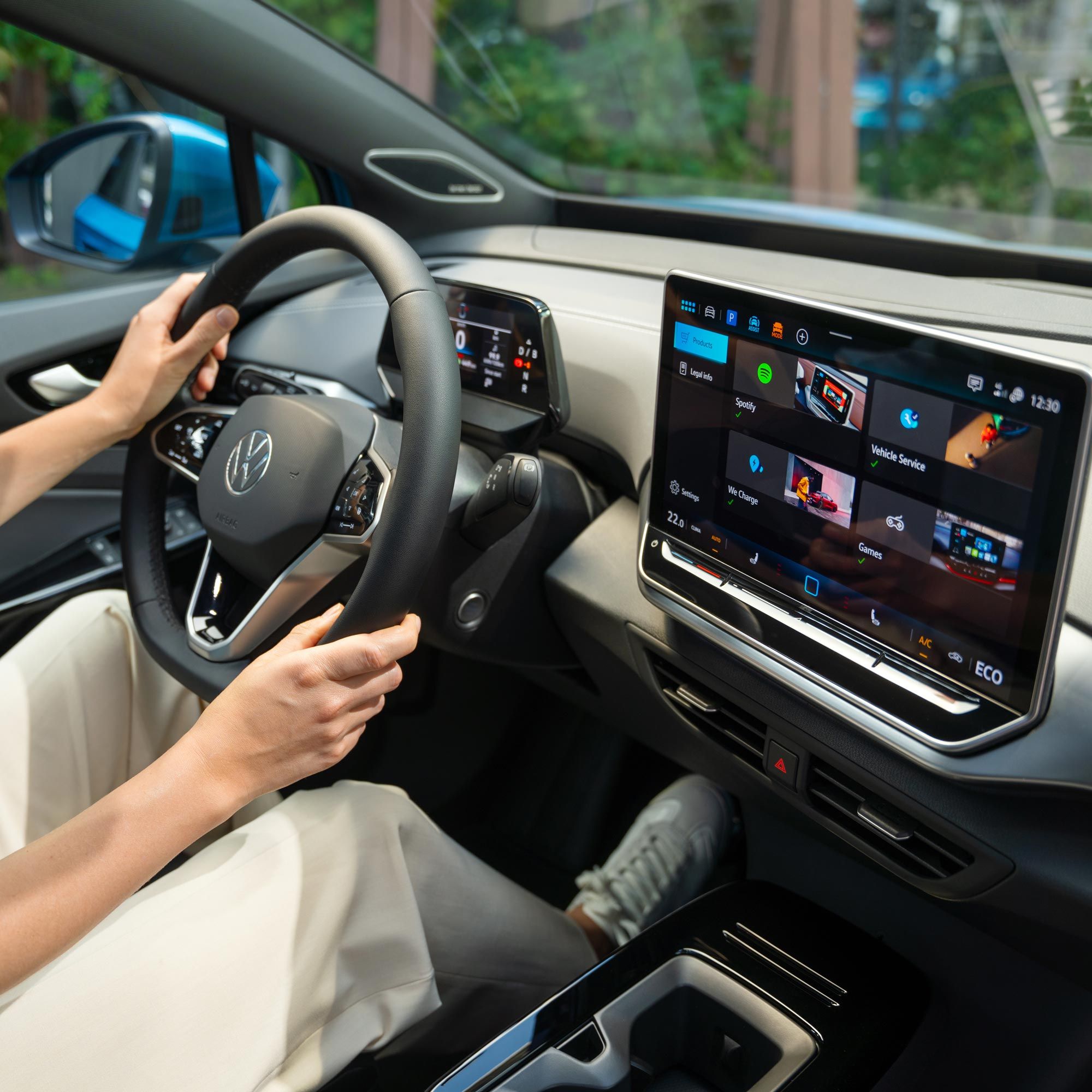 Innenansicht des VW ID.4. Schräger Seitenblick  auf das Multifunktionslenkrad und Infotainmentsystem. Auf dem Fahrersitz sitzt eine Person, die das Fahrzeug lenkt. 