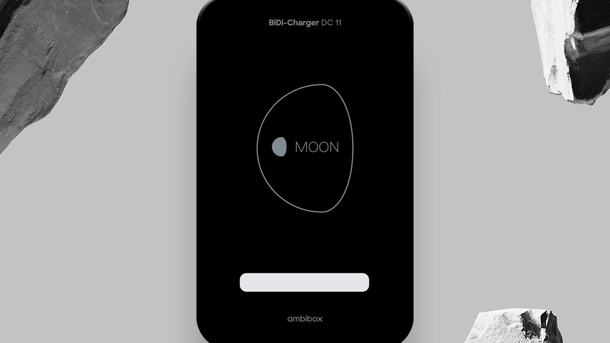 Ein BiDi-Ladegerät DC 11 mit einem eleganten schwarzen Design und dem Schriftzug "MOON" in der Mitte, umgeben von einer Kontur. Es befindet sich vor einem grauen Hintergrund mit zwei großen, strukturierten Steinen an den Seiten.