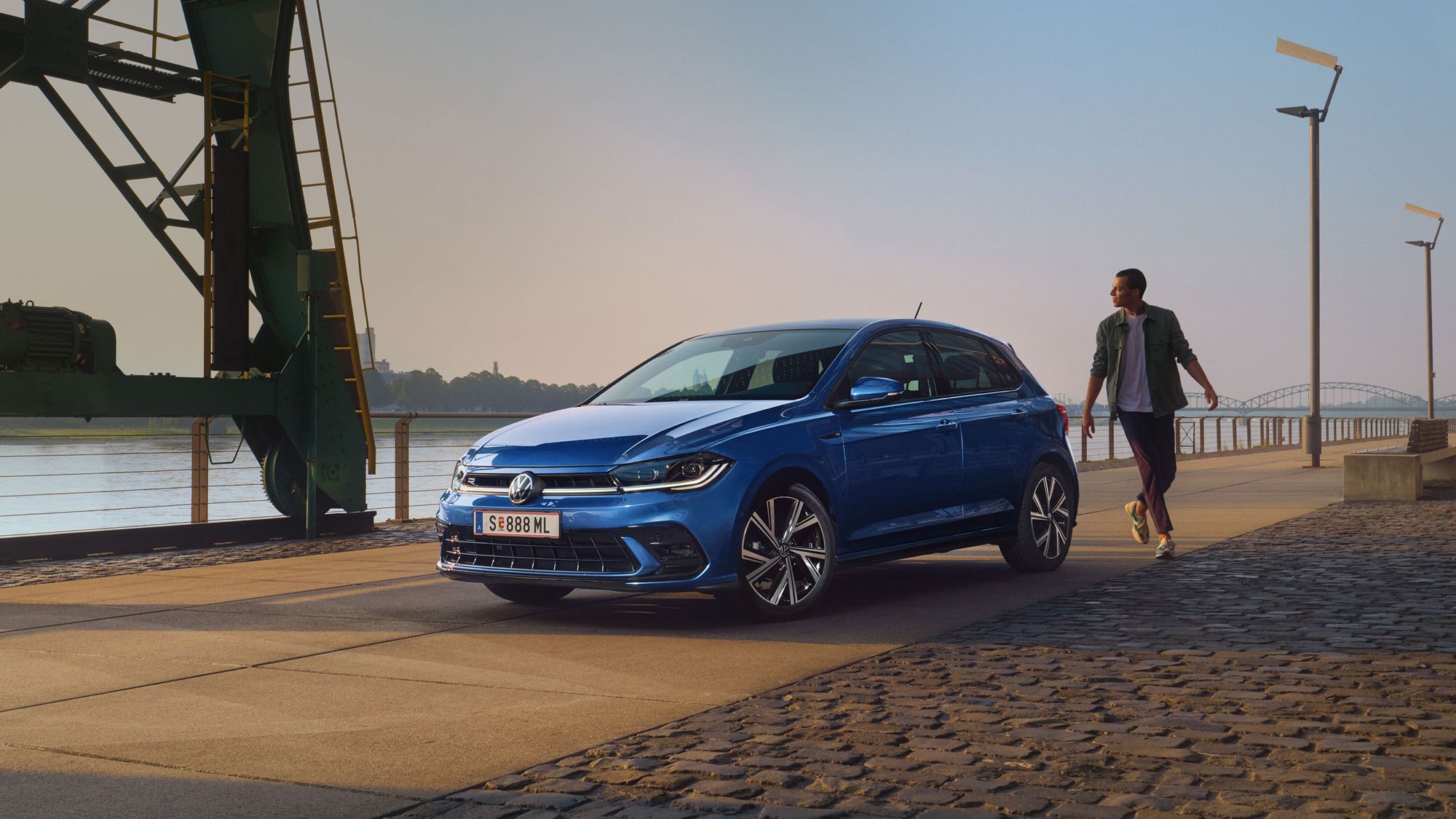 Mann geht an blauen VW Polo R-Line vorbei, der an Promenade geparkt ist