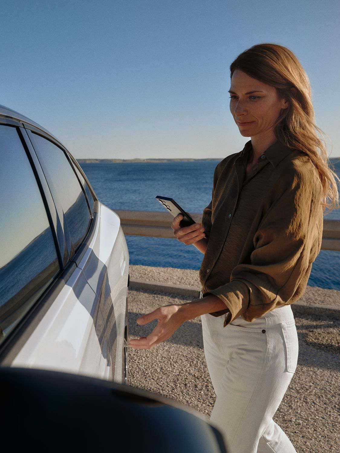 Eine Frau geht zu einem weißen VW ID.7 und öffnet die Tür. 