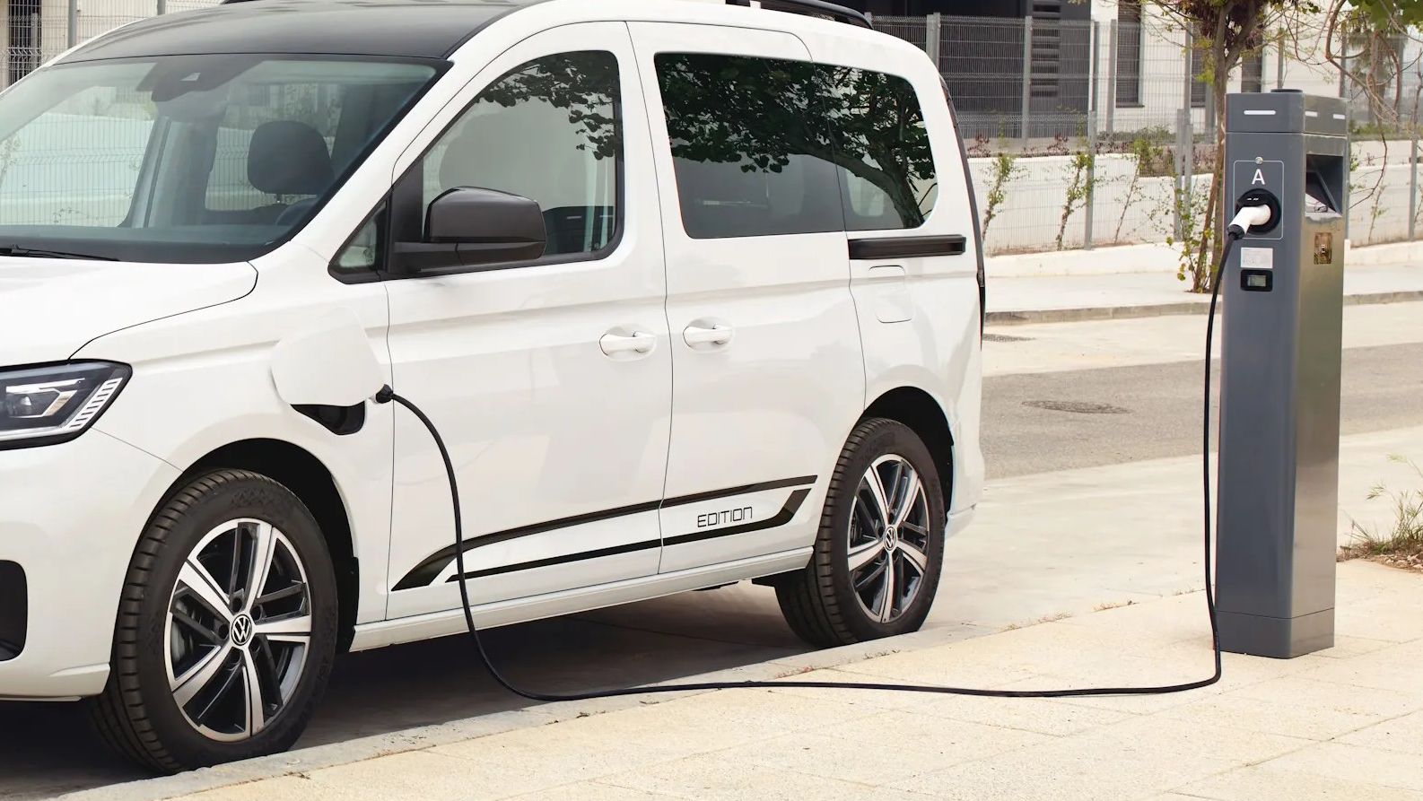Ein weißer VW Caddy eHybrid steht an einer Ladesäule.