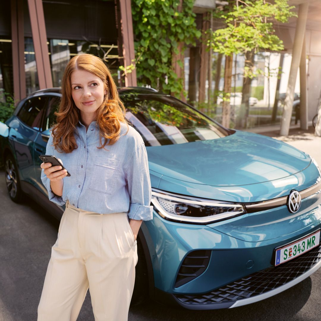 Frau steht mit einem Handy in der Hand vor dem ID.4 