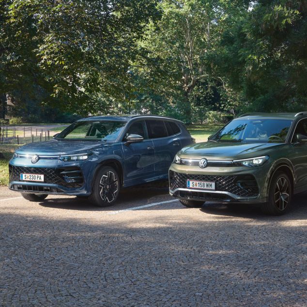 Blauer Tiguan R-Line Plug-In-Hybrid und grüner Tayron R-Line Plug-In- Hybrid parken nebeneinander im schattigen Parkbereich.
