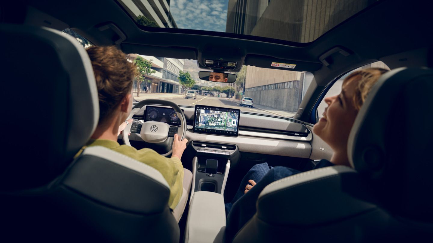 Ein Mann fährt einen VW ID. Polo Style, auf dem Beifahrersitz eine Frau die lacht. Durch das Panoramadach sind Hochhäuser zu sehen