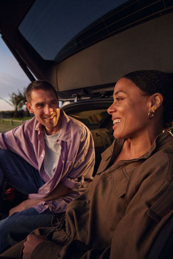Ein Mann und eine Frau sitzen unter der geöffneten Heckklappe eines Volkswagen ID.7 Tourers