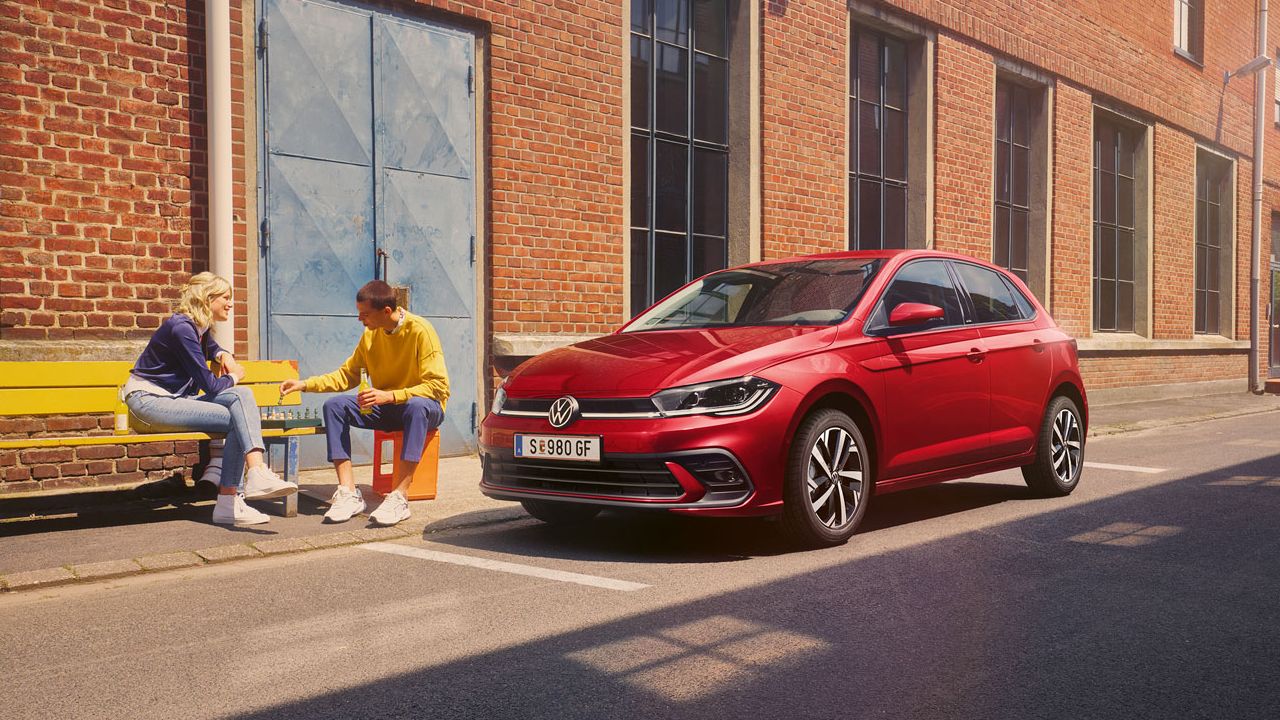 Zwei Personen spielen Schach vor einem roten VW Polo Style, der vor einem Fabrikgebäude parkt.