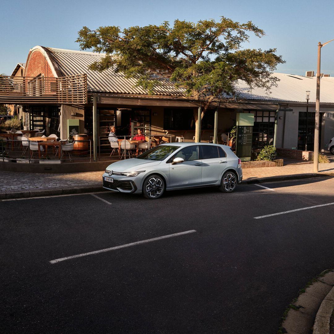 Seitenansicht eines grauen VW Golf, der vor einem Lokal parkt.