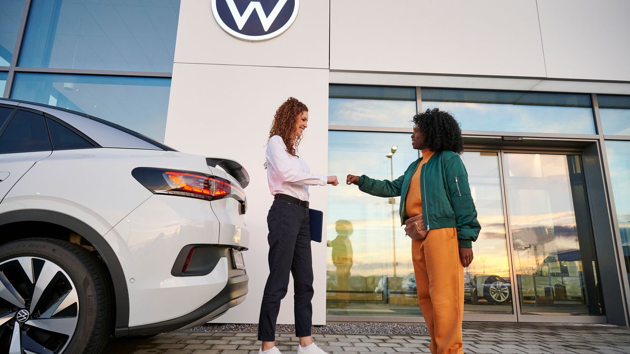 Eine Volkswagenmitarbeiterin und eine Kundin verabschieden sich vor einer Volkswagen Werkstatt.