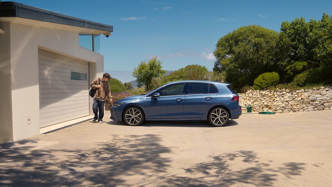 Ein junger Mann geht an einem blauen VW Golf vorbei