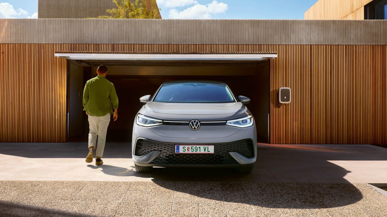 Ein grauer VW ID.5 steht vor einer Garage mit geöffnetem Tor. Ein Mann geht darauf zu.