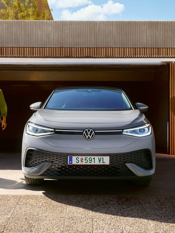 Ein grauer VW ID.5 steht vor einer Garage mit geöffnetem Tor. Ein Mann geht darauf zu.