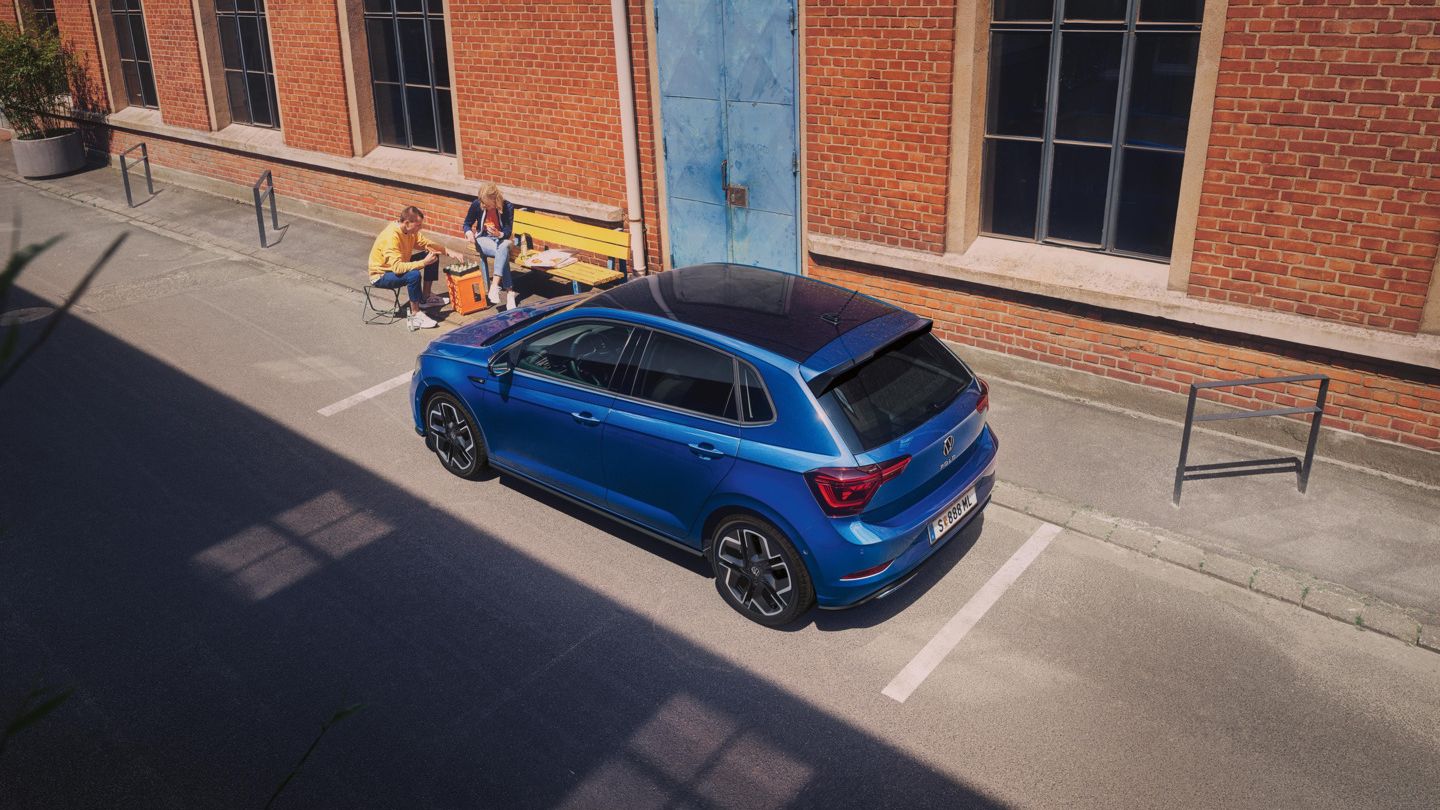 Blick von schräg oben auf einen parkenden VW Polo R-Line mit Roof-Pack, neben dem Auto spielt ein Pärchen Schach.