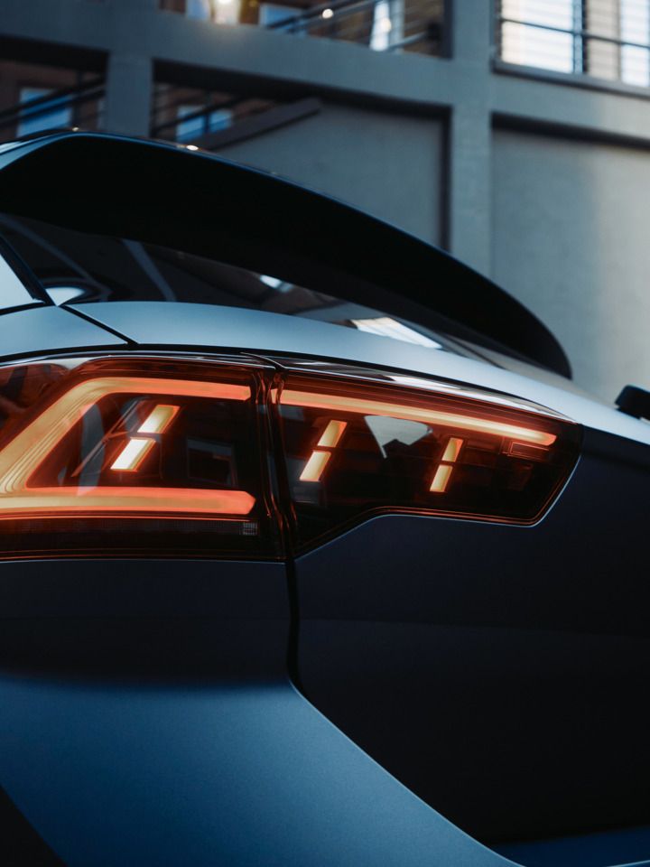 Nahaufnahme des Rücklichts eines modernen Autos, möglicherweise eines Volkswagen. Das Fahrzeug steht vor einem städtischen Hintergrund. Die Beleuchtung der Rücklichter ist eingeschaltet.