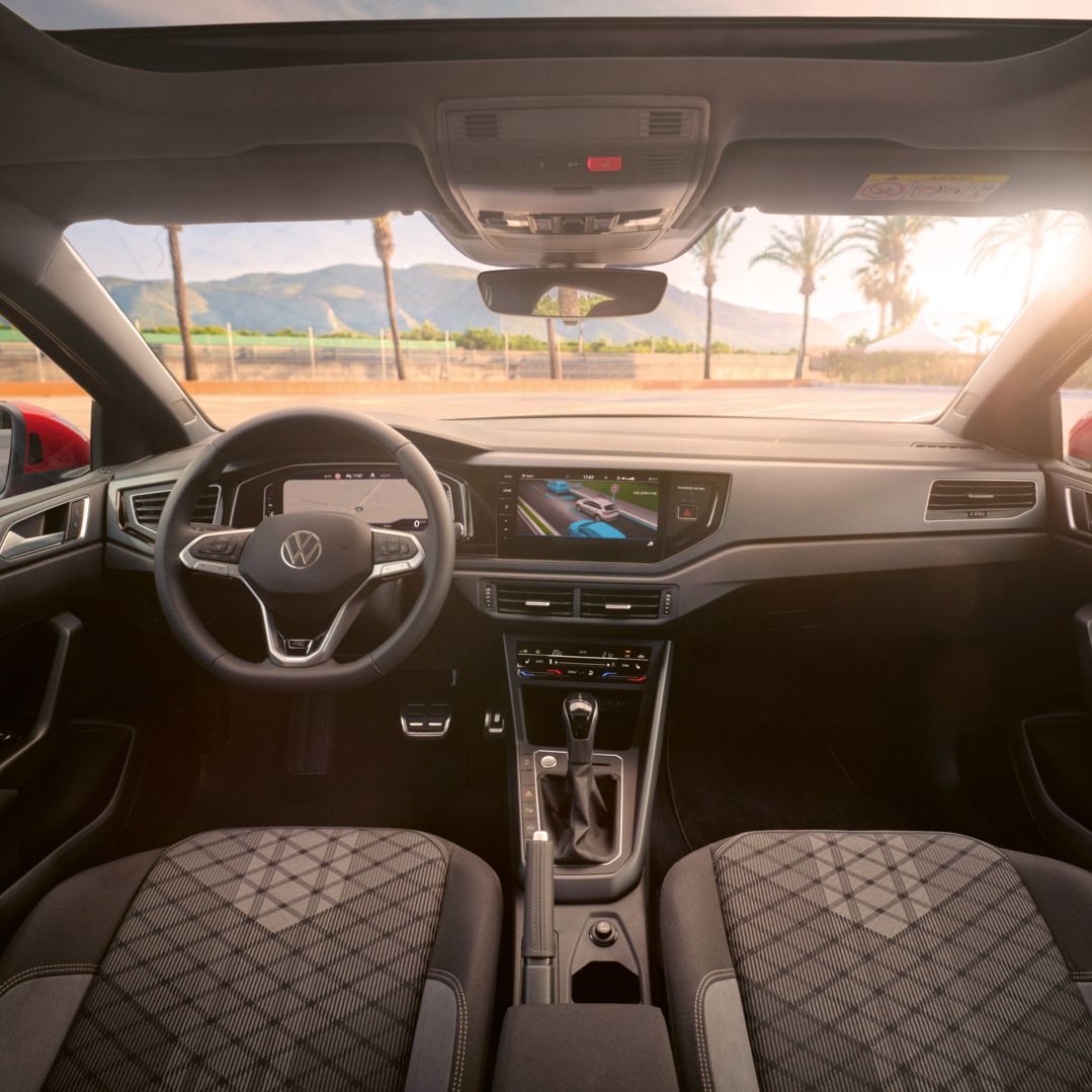 Blick auf das Cockpit mit Lenkrad und Infotainment-System im VW Taigo. Vor dem Fahrzeug sind Palmen und Berge.