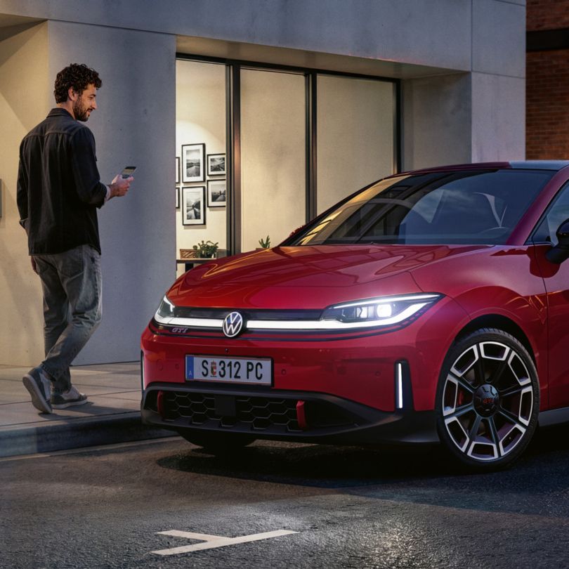 Eine Person geht an einem roten VW ID. Polo GTI vorbei, der vor einem modernen Gebäude parkt.